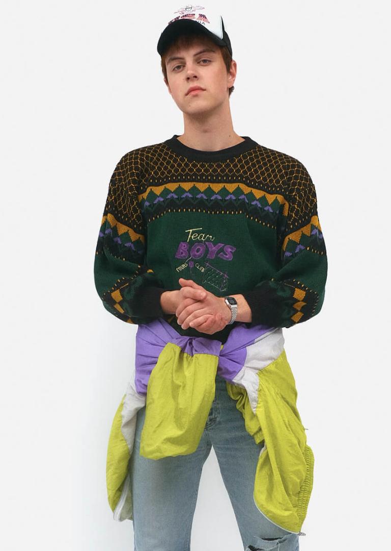 Чоловік у візерунчастому светрі «Team Boys», джинсах та бейсболці в стилі 90-х років на білому фоні