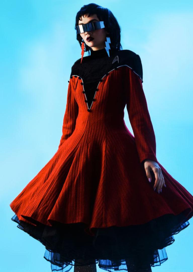 Жінка у червоній футуристичній сукні з чорним під'юбником, кіберпанк-окулярах та сережках у формі блискавок