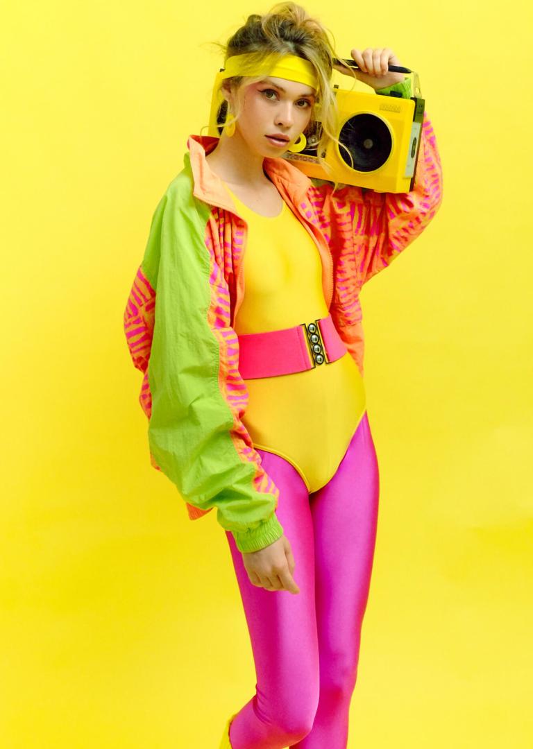 Жінка в неоновому спортивному вбранні з бумбоксом на плечі у стилі 90-х років на жовтому фоні