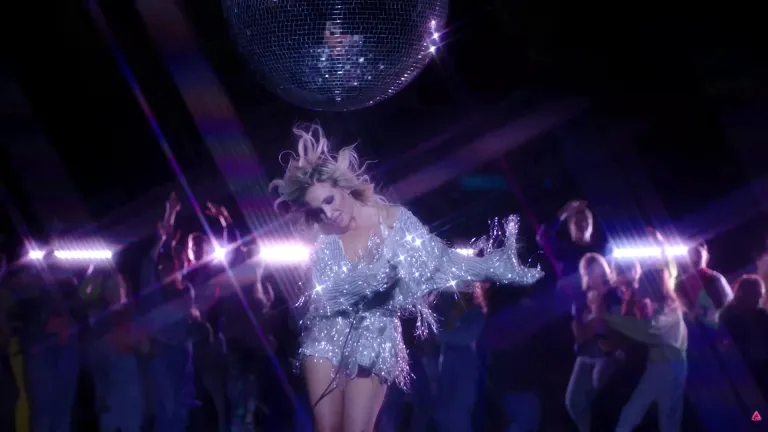 Дівчина в блискучій сріблястій сукні танцює під диско-кулею у нічному клубі